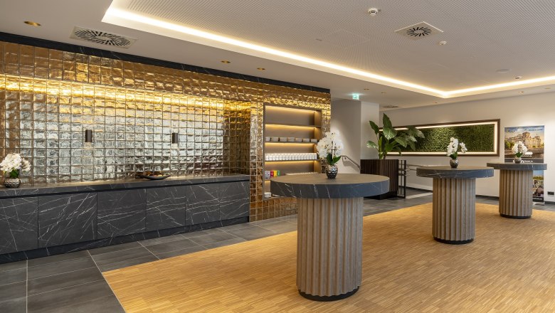 Modern room for seminar coffee breaks with a golden wall, black marble tables and orchids.