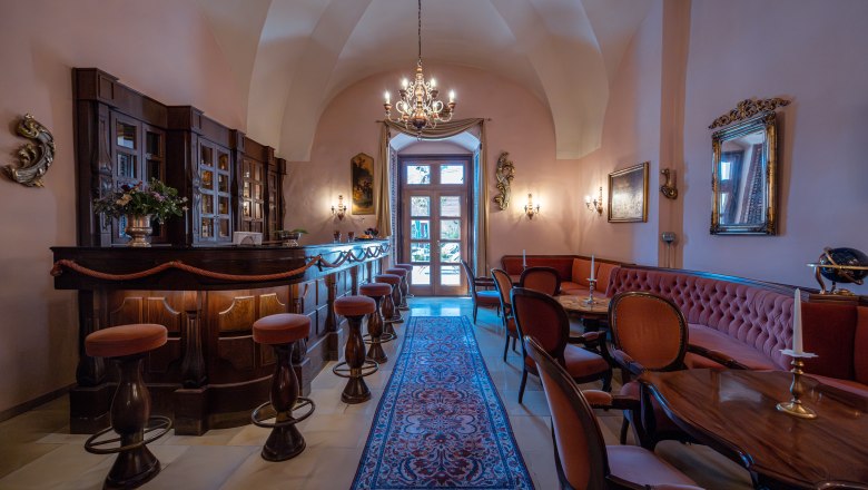 Elegant interior of a hotel bar with wooden furniture, chandelier and carpet.