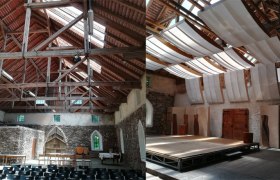 Interior view of a historic building with wooden roof and stage.