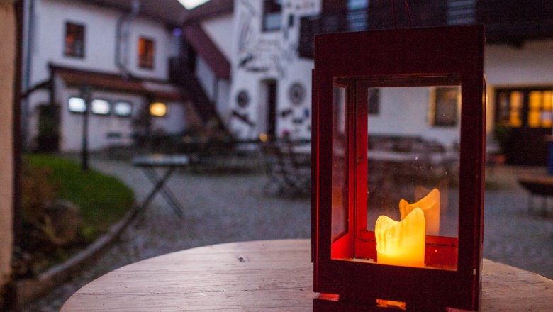 Lantern with a burning candle on a wooden table in the courtyard of a country hotel.
