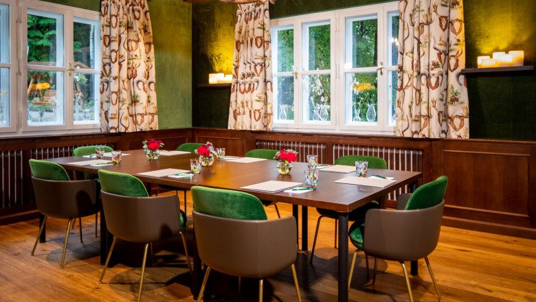 A hunting room with a wooden table, green chairs and antler chandelier.