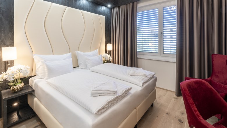 Modern hotel room with double bed, red armchairs and large windows with curtains.