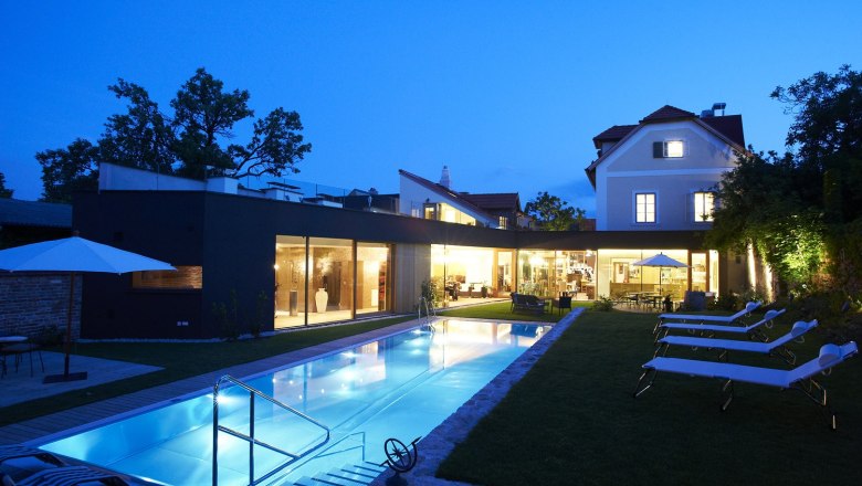 Evening view of a modern hotel with illuminated pool and sun loungers in the garden.