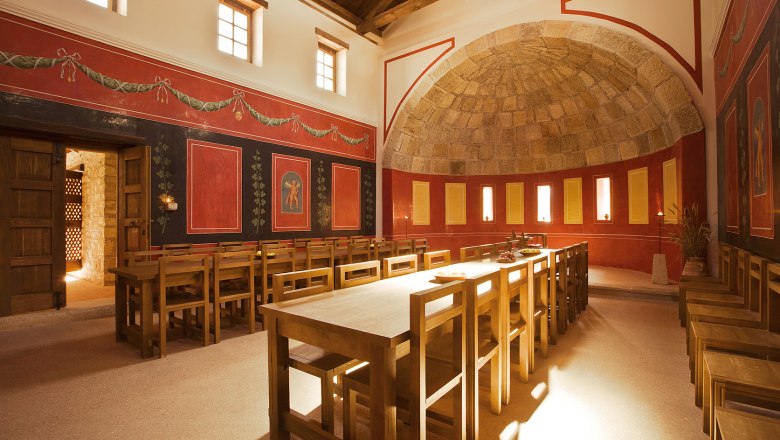 Interior view of a Roman dining room with wooden tables and chairs, red walls and decorative frescoes.