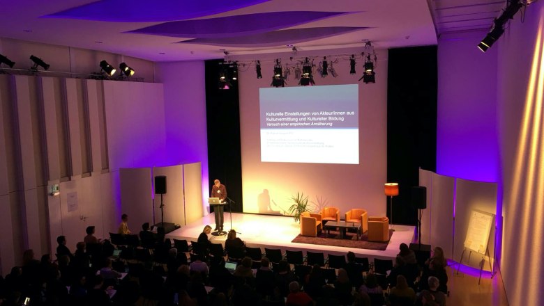 A lecture in a conference room with purple lighting and an audience.