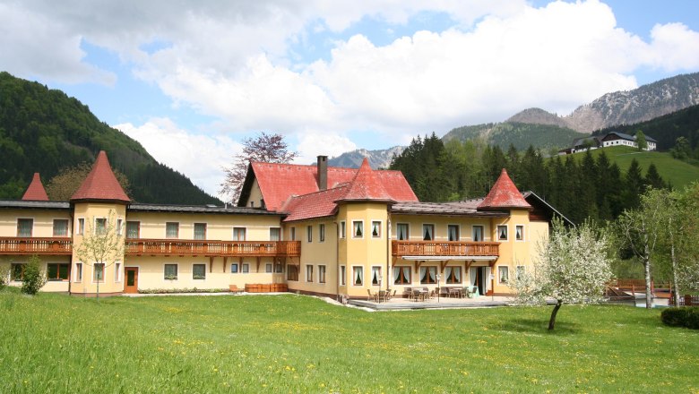 A large hotel with red roofs in a green, mountainous landscape.
