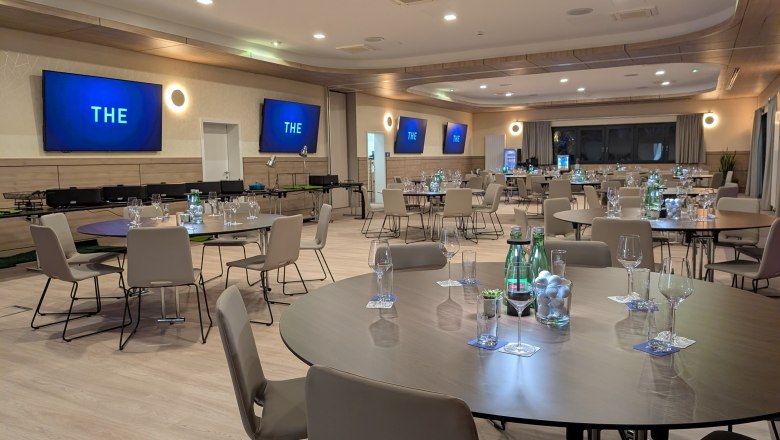 Modern seminar room with round tables, chairs and screens on the walls.