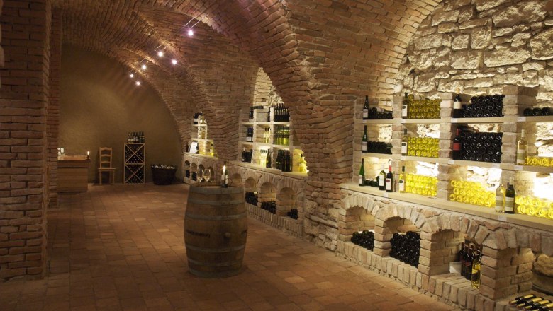 Wine cellar with brick vaults and wine bottles on shelves.