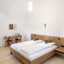 A simply furnished guest room with a double bed, wooden furniture and a cross on the wall.