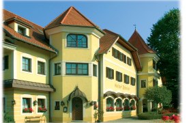 Yellow building with red roofs and many windows, surrounded by trees.