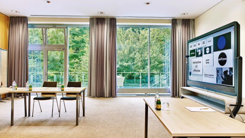 Modern seminar room with large windows, tables, chairs and an interactive screen.