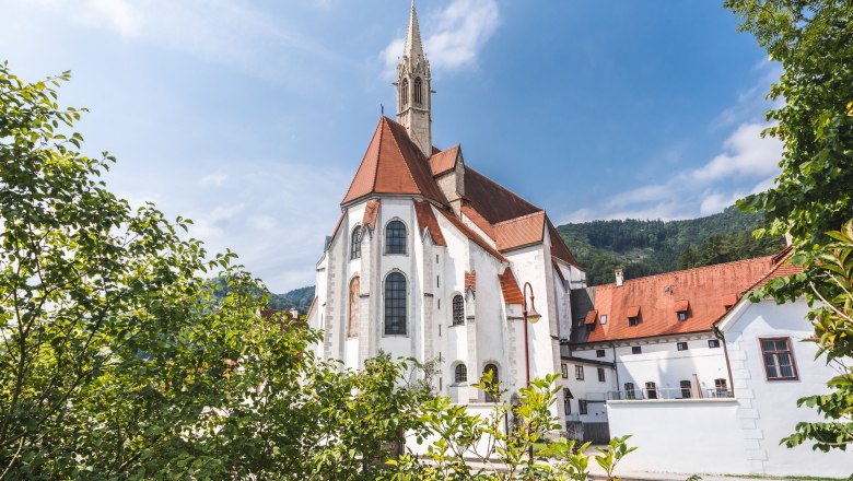 Historic building with red roof and tower, surrounded by trees.