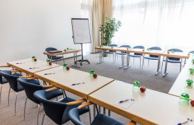 Conference room with U-shaped tables, chairs, flipchart and writing materials.