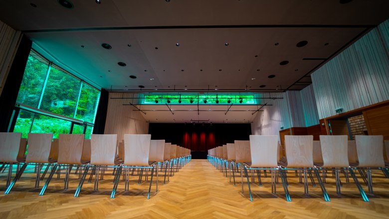Interior view of a modern event room with empty rows of chairs and a stage in the background.