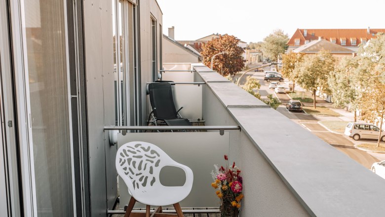 Balcony with white chair and bouquet of flowers, view of the street and building.