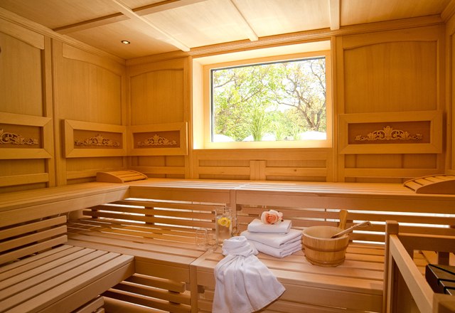 Interior view of a sauna with wooden benches, towels and a window with a view of the greenery.