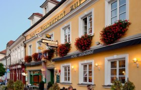 Facade of a yellow building with the lettering 'Hotel-Restaurant zur Post'. People are sitting at tables in front of the building.
