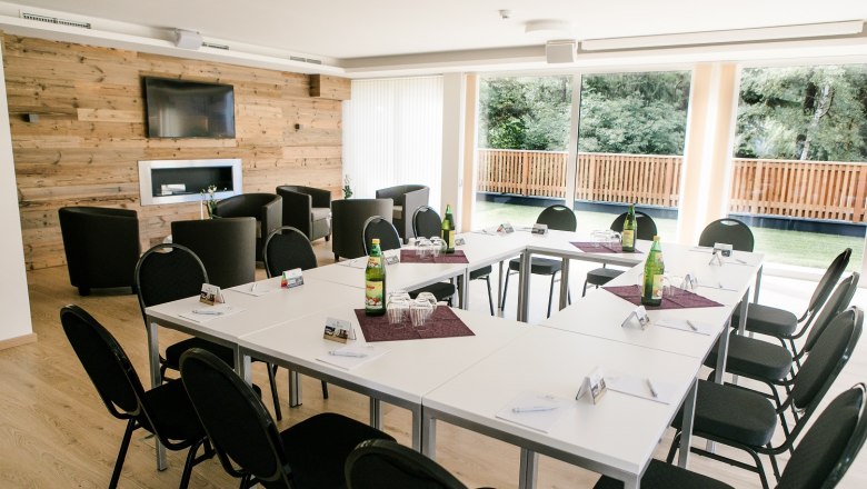 Conference room with U-shaped table arrangement, chairs, wooden wall, TV and large windows with a view of the greenery.