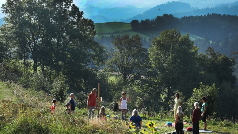 Group of people doing yoga outdoors in front of a picturesque mountain landscape.