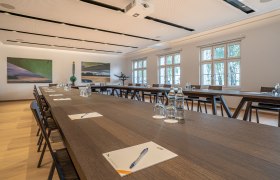 Seminar room in the Hotel Spitzerberg with long wooden tables, chairs, water bottles and writing materials.