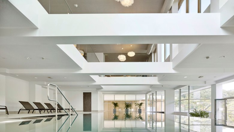 Indoor pool with sun loungers and large windows.
