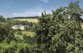 A hotel building in the middle of a green landscape with trees and hills in the background.