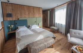 Modern hotel room with double bed, wooden walls and large windows.