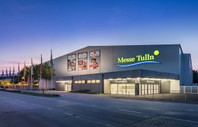 Exterior view of Messe Tulln at dusk with illuminated entrance and flags.