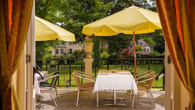 View of a terrace with yellow parasols and a laid table, surrounded by green countryside.