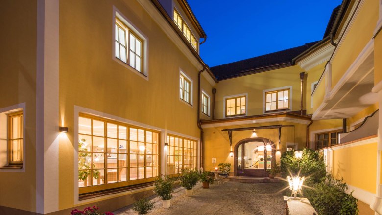 Inner courtyard of the Hotel Zum Schwarzen B&auml;ren with illuminated windows and plants at night.