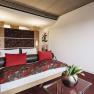 Modern hotel room with double bed, red cushions and floral pattern. A glass coffee table with a vase full of tulips stands in the foreground.