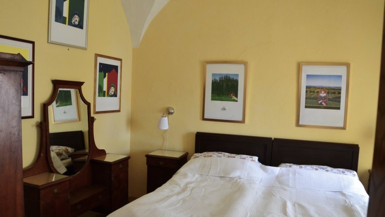 Bedroom with double bed, yellow walls and several framed pictures on the wall.