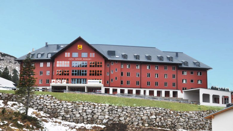 Large red building of the Jufa Sport Resort in a mountainous landscape.
