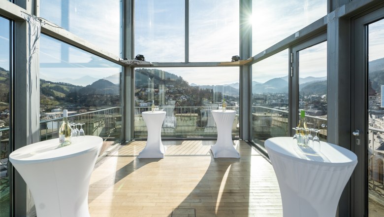 Interior view of a modern glass room with bar tables and mountain views.
