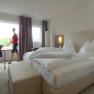 Modern furnished hotel room with double bed, large window and a person walking by.