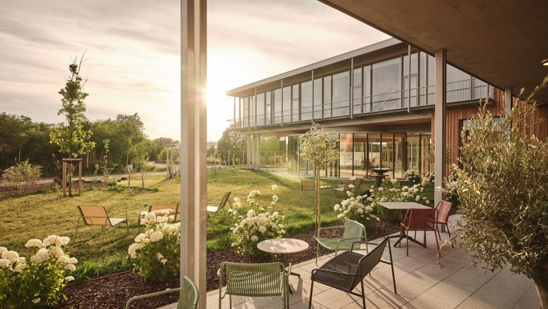 A modern patio with patio furniture and flowers in front of a building at sunset.