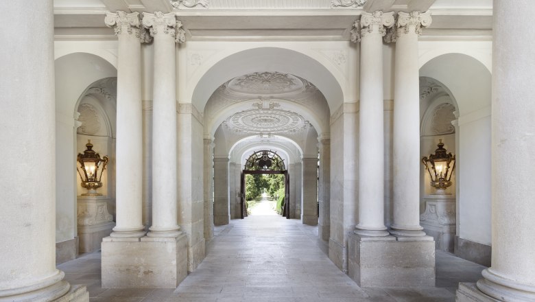 Elegant, column-lined passageway in Eckartsau Castle with ornate ceilings and wall lights.