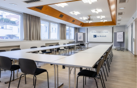 Seminar room at Das Reinisch Hotel with tables, chairs and presentation screen.