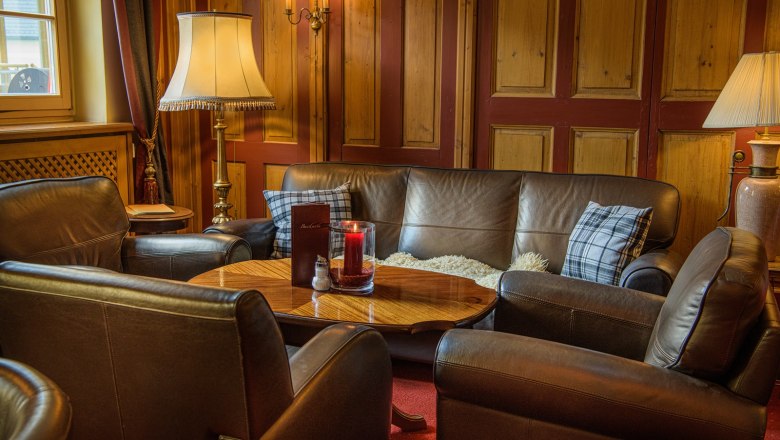Cozy bar area with leather sofas, wooden table and lamps.