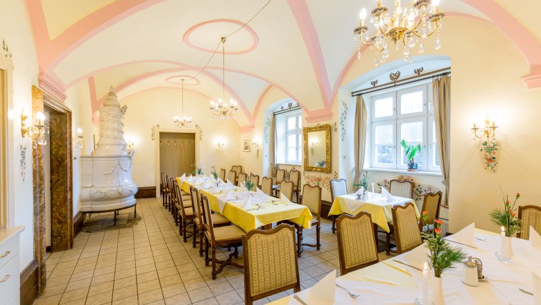 Elegant dining room with laid tables, chandeliers and tiled stove.