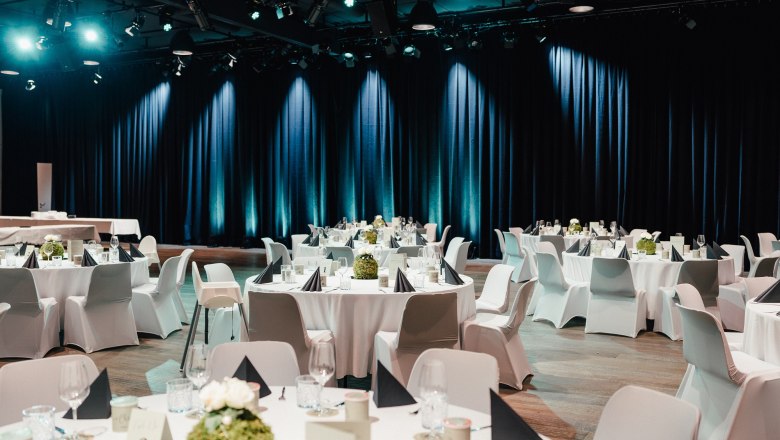 Elegant gala seating with round tables, white tablecloths and black napkins in a festively lit hall.