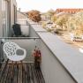 Balcony with white chair and bouquet of flowers, view of the street and building.