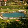 A natural swimming pond with sun loungers and colorful parasols on a green meadow.
