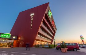 Modern hotel building with sloping façade and illuminated lettering 'ibis HOTEL'.
