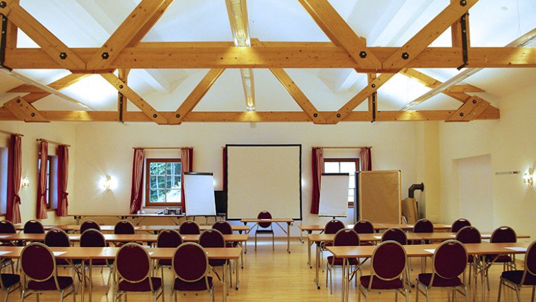 Seminar room with wooden beamed ceiling, tables and chairs, screen and flipcharts.
