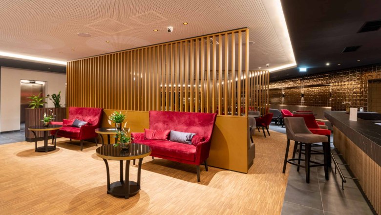 Modern hotel lobby with red sofas, wooden walls and plants.