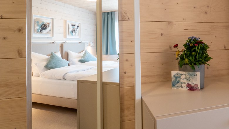 A cozy bedroom with wooden walls, a bed with blue pillows and a small table with a plant and a map.