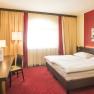 A cozy hotel room with a double bed, red carpet, desk, TV and modern art on the wall.