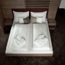 A modern hotel room with a double bed, white comforters and bathrobes, surrounded by wooden furniture.