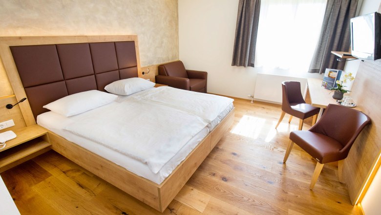 Modernly furnished hotel room with double bed, desk, chairs and an armchair.